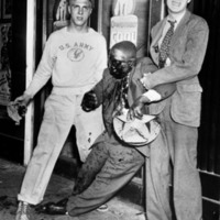Two men pose while holding a brutalized man